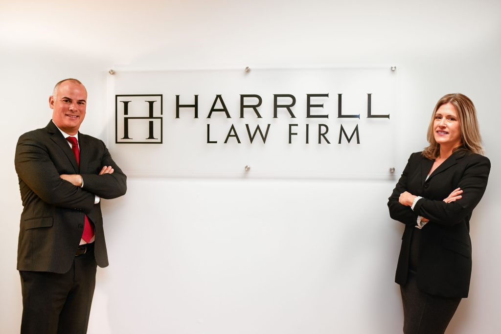 Ken Harrell and Leigh Raffauf standing in front of a Harrell Law Firm sign