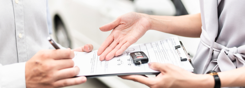 An insurance adjuster showing a document on a clipboard to a driver