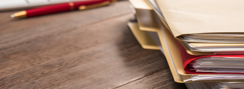 A stack of manila folders on a desk with papers inside