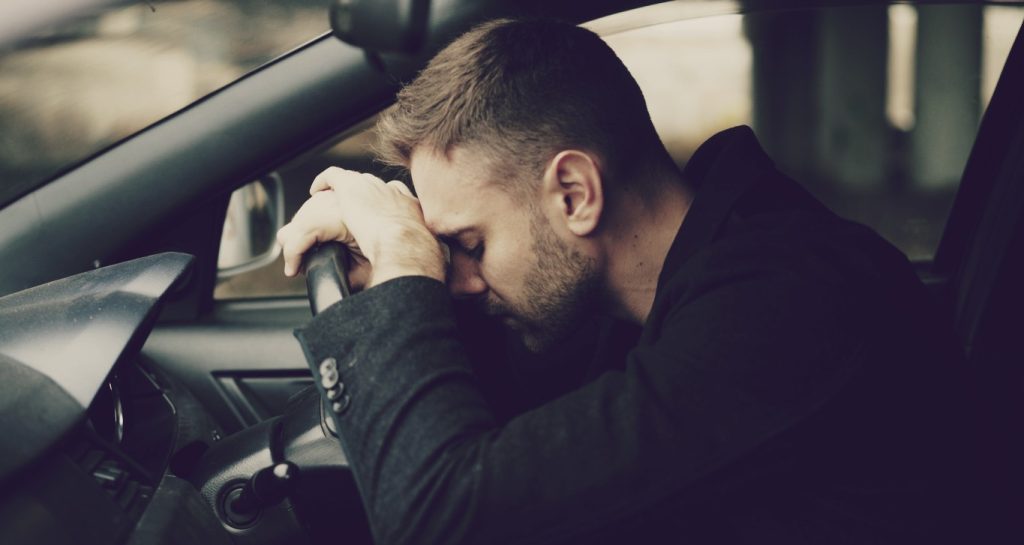 Man in car with head over steering wheel