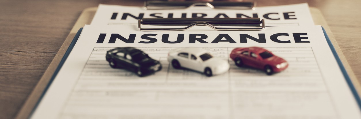 Three toy cars sitting on an insurance form and clipboard.