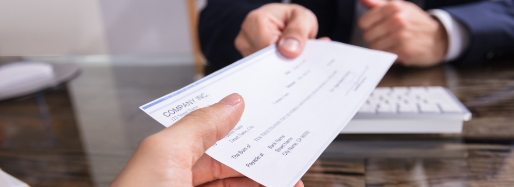 Close-up Of A Businessperson's Hand Giving Cheque To Colleague At Workplace