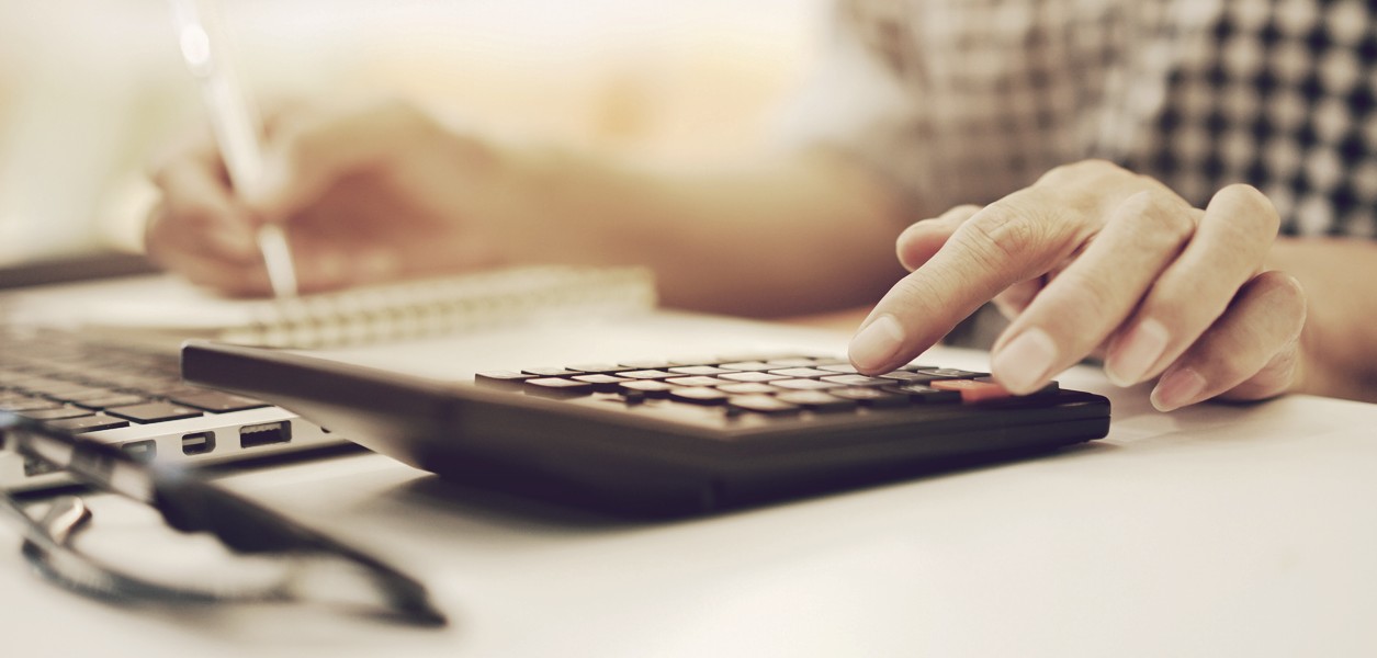 Person calculating on a calculator, and laptop.