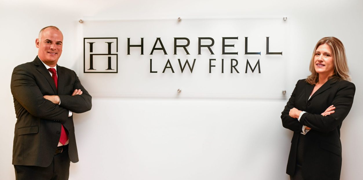 Ken Harrell and Leigh Raffauf standing in front of a Harrell Law Firm sign